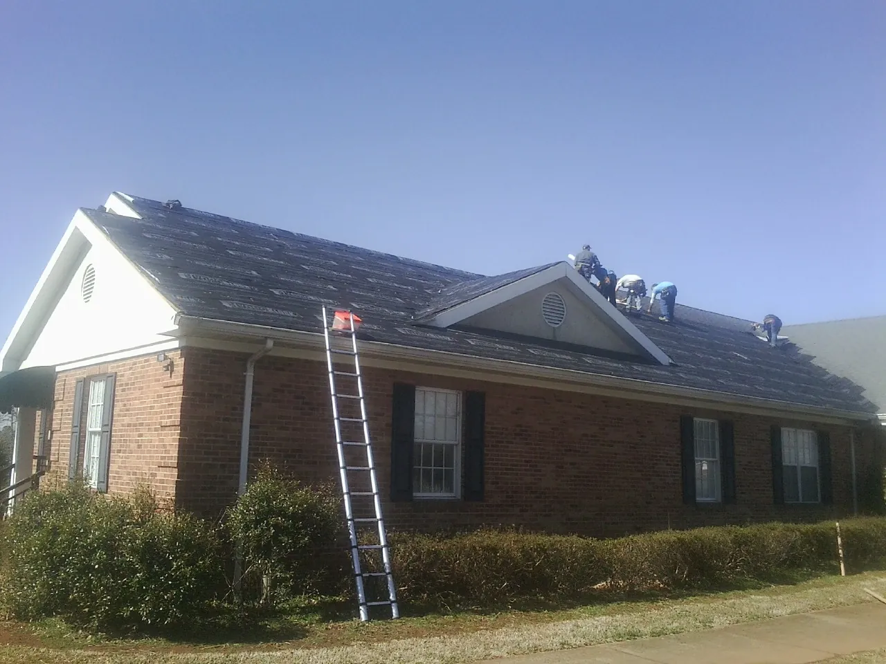 Crew tearing shingles off a brick ranch roof with a ladder set — Metal Roof Repair work by our crew in Rochester